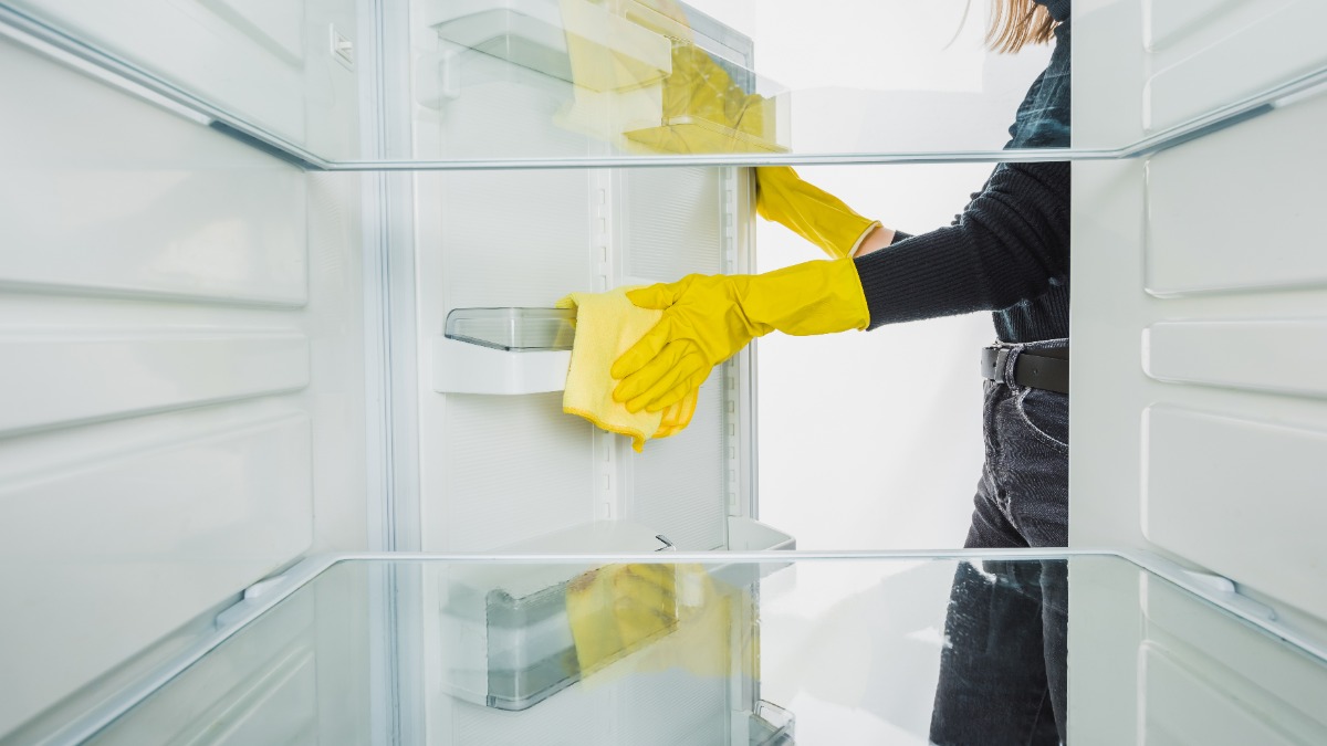eine Frau wischt einen leeren Kühlschrank sauber