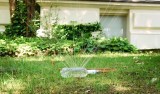 Ein selbst gebauter Rasensprenger aus einer Plastikflasche bewässert einen Rasen in einem Garten.