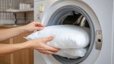 Ein Sofakissen wird in eine Waschmaschine gesteckt.