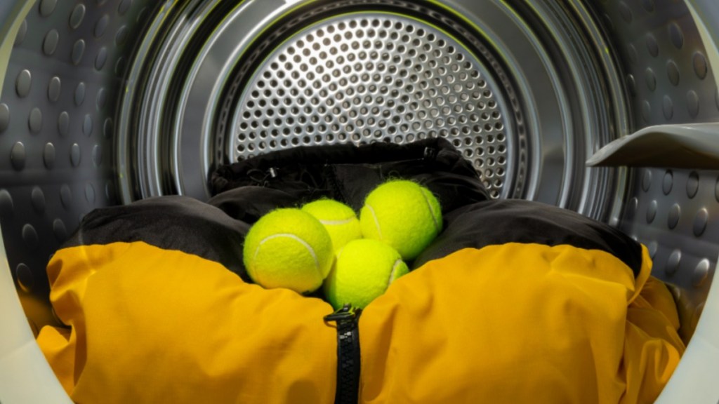 Tennisbälle liegen in einer Waschmaschine auf einer Daunenjacke.