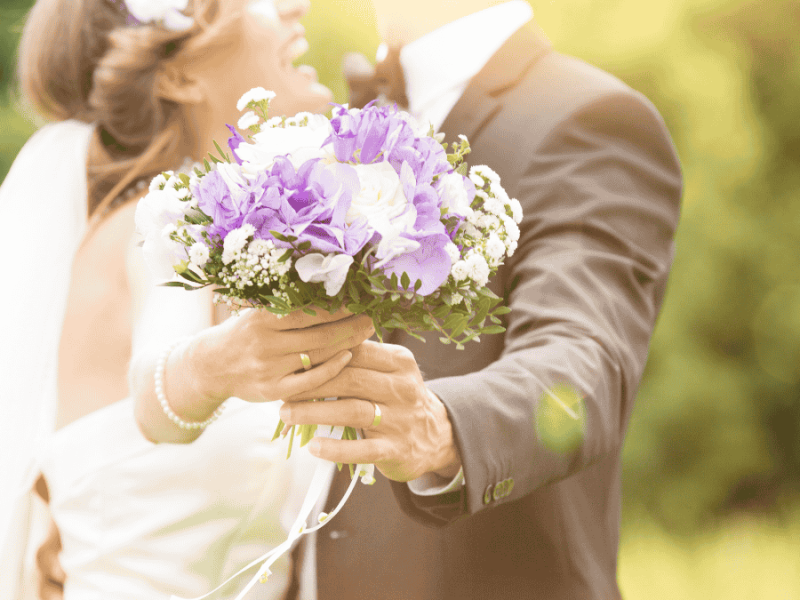 wie viel geld zur hochzeit schenken, Brautpaar hält Brautstrauß in die Kamera