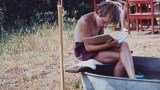 Aufnahme eines Jungen im Jahr 1960, der ein Buch liest, während er auf dem Rand einer Zinnwanne sitzt