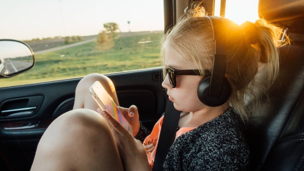 ein Mädchen sitzt mit Kopfhörern und Handy im Auto