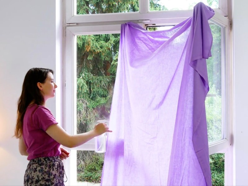 Eine junge Frau hängt ein violettes, feuchtes Tuch in ein Fenster, als Maßnahme gegen Hitze.