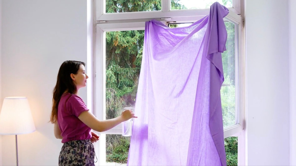 Eine junge Frau hängt ein violettes, feuchtes Tuch in ein Fenster, als Maßnahme gegen Hitze.