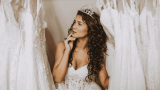 Hochzeitskleid kaufen, Braut steht zwischen Hochzeitskleidern und guckt fragend