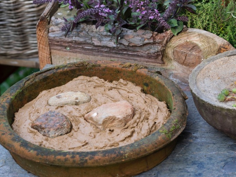 Eine Schüssel mit Lehm in einem Garten. Mit dieser Nisthilfe unterstützt du Insekten, Bienen und Vögel.