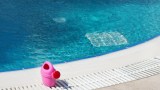 eine rosafarbene Kindergießkanne steht an einem Pool