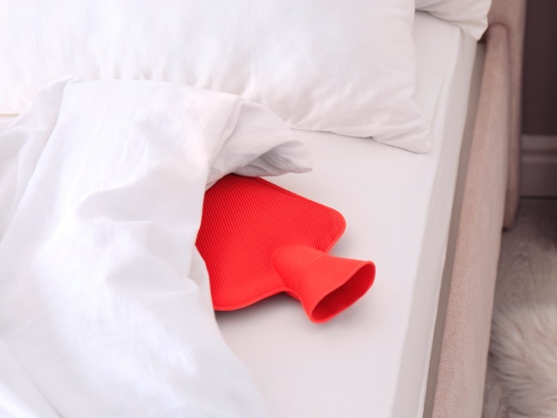 Rote Wärmflasche in einem Bett.