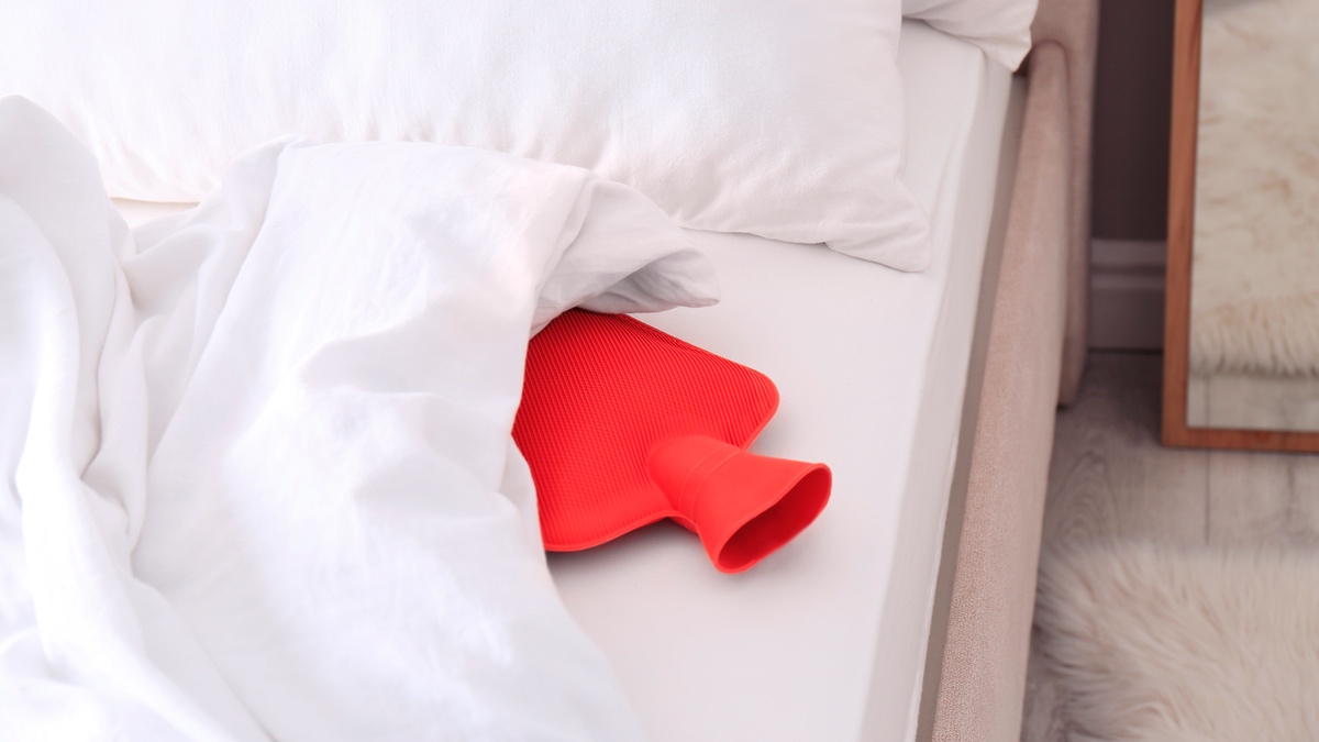 Rote Wärmflasche in einem Bett.