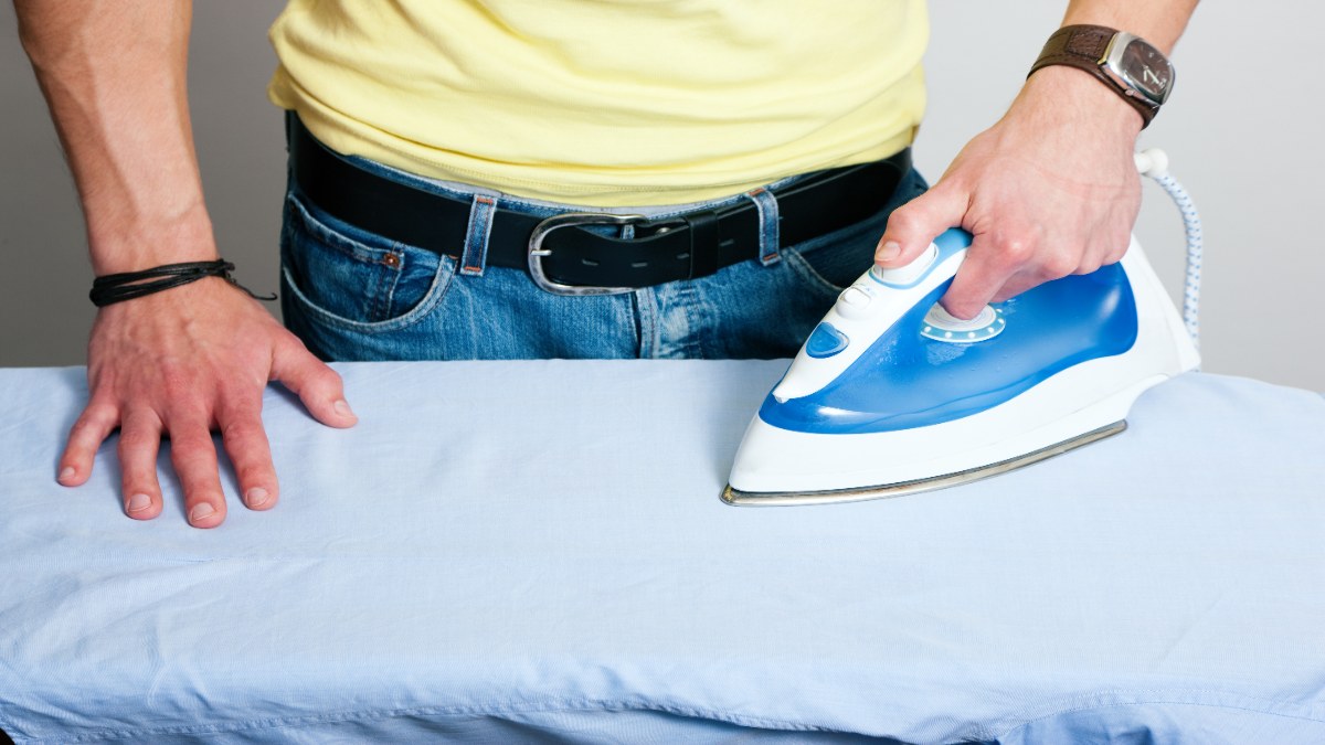 Mann in Jeans bügelt.